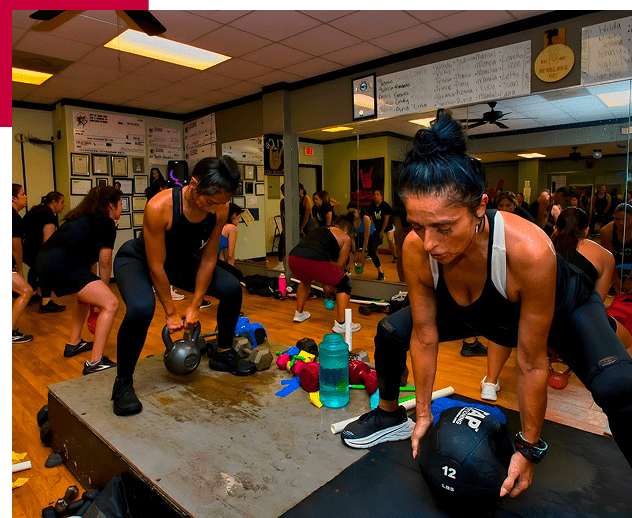 Women working out intensely with kettlebells in a gym session.