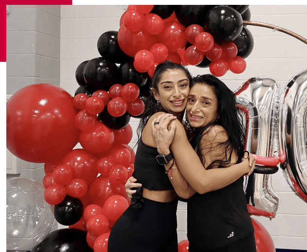Two women happily hugging in front of red and black balloons.